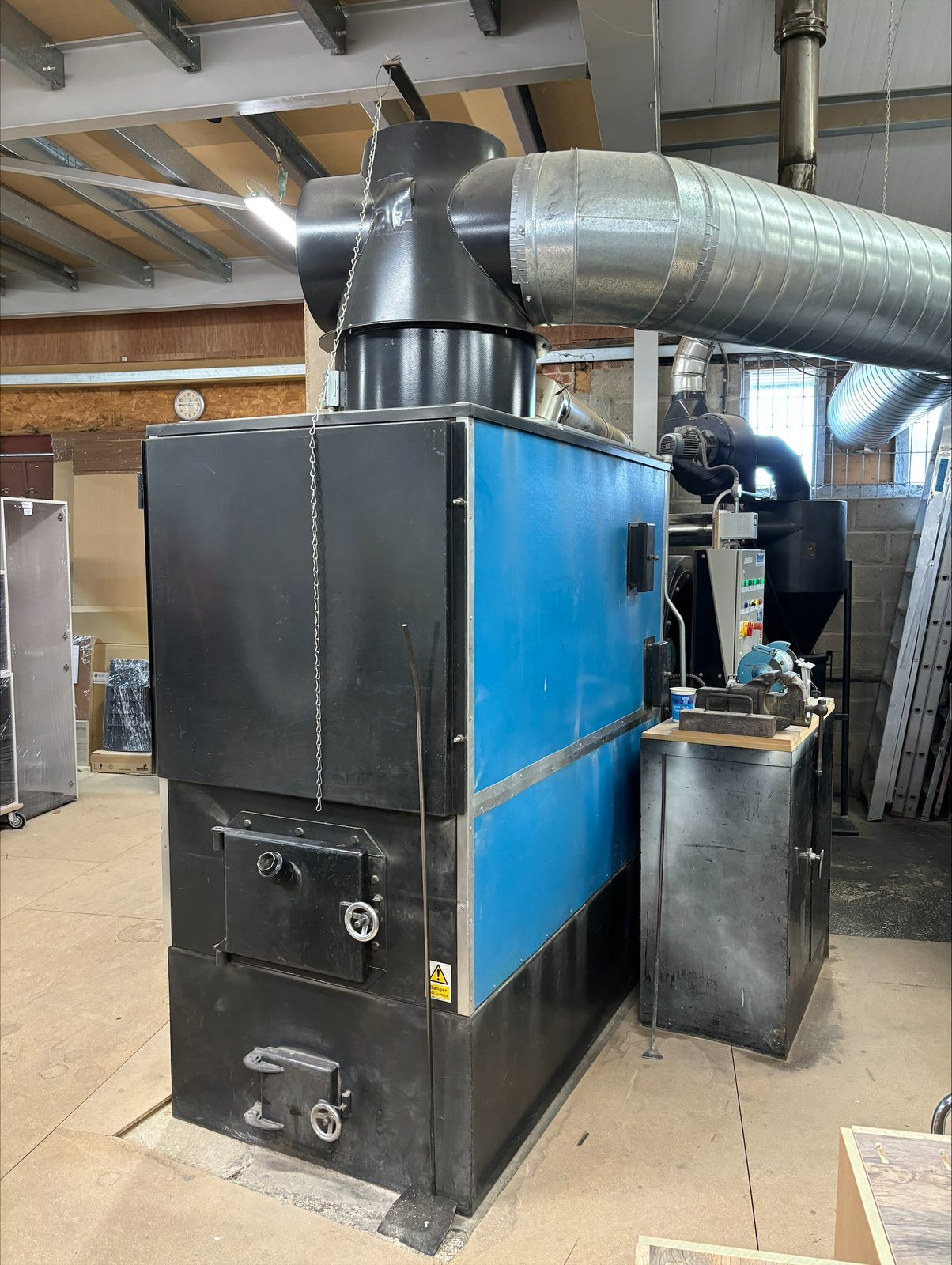 Front view of a 17-year-old Ranheat WA 150 wood waste warm air heater showing the black cast fuel and ash doors and blue heater body