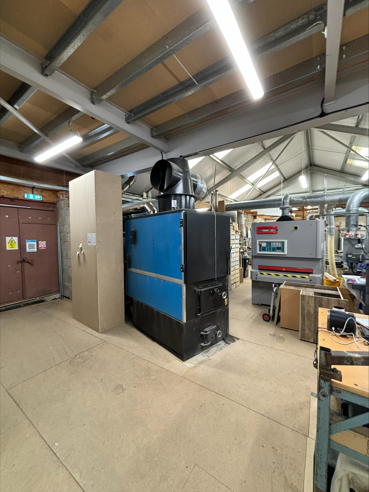 Wide view of a 17-year-old Ranheat WA 150 wood waste warm air heater installed in a working timber workshop
