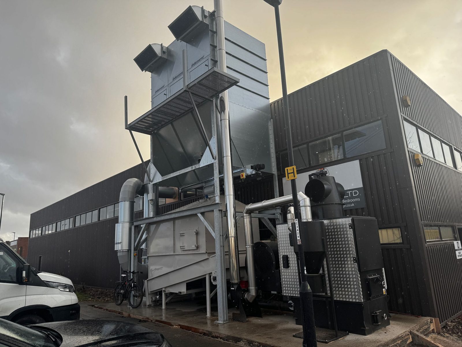 Wide site view of a Ranheat WA 150 warm air heater installation with galvanised B10 bunker silo, elevated dust extraction filters and chimney