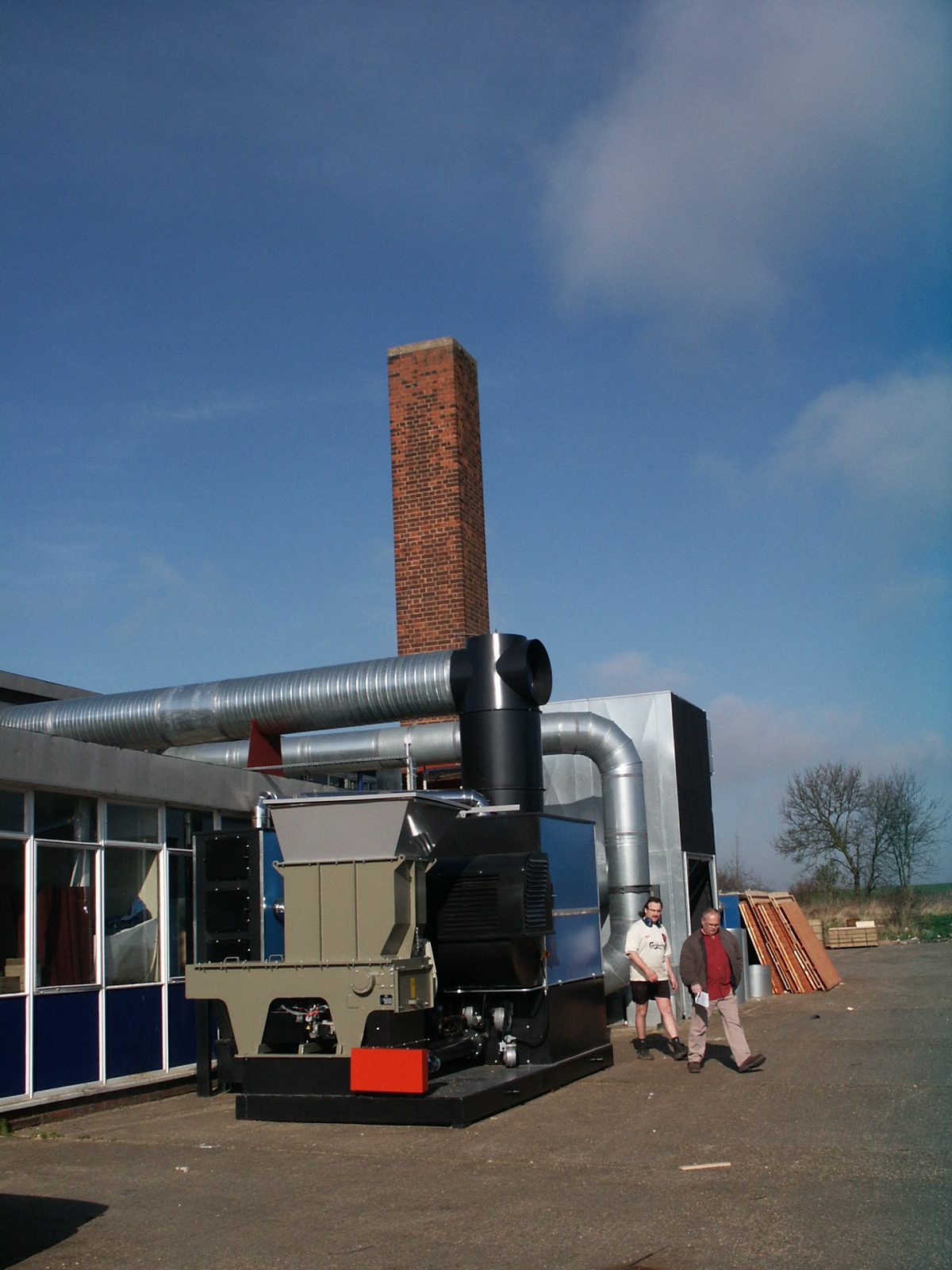 Installed Ranheat WA 300 warm air heater with hogger loader and galvanised ducting against a tall brick chimney